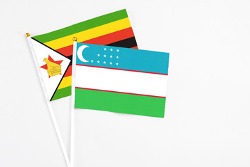 Uzbekistan and Zimbabwe stick flags on white background. High quality fabric, miniature national flag. Peaceful global concept.White floor for copy space.