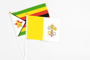 Vatican City and Zimbabwe stick flags on white background. High quality fabric, miniature national flag. Peaceful global concept.White floor for copy space.