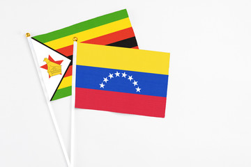 Venezuela and Zimbabwe stick flags on white background. High quality fabric, miniature national flag. Peaceful global concept.White floor for copy space.