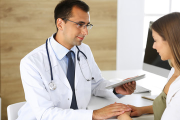 Doctor reassuring her female patient because of her first pregnancy fear while sitting at a desk in...