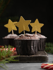 Christmas and new year chocolate muffins decorated with big golden stars, fir tree brances, dark background