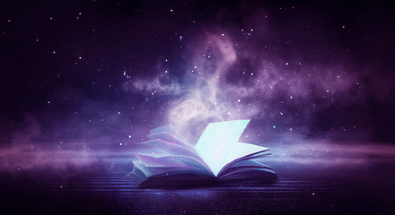 An open book on a wooden table under the night sky against a dark forest. Magical radiance. Night scene. © MiaStendal