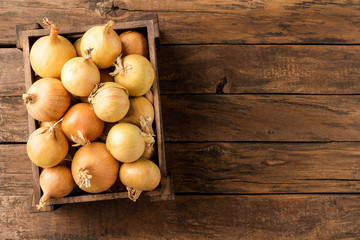 Overhead shot of fresh white onions in crate on rustic wooden table with copyspace