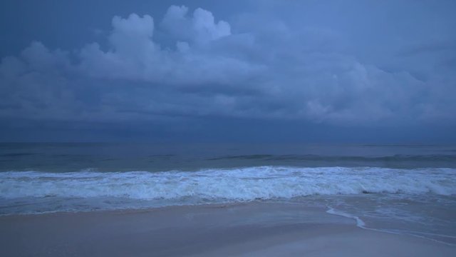Sea waves crash as amazing, epic purple lightning strikes fill the ocean sky and illuminates the saltwater drenched clouds as a dangerous storm warns of bad and adverse weather fast approaching.