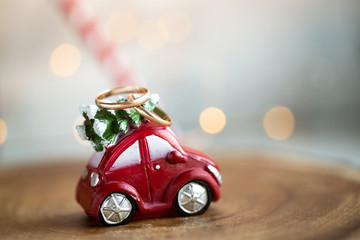 Red toy car with a christmas tree on the roof and two wedding ring, with bokeh on background. new year wedding concept