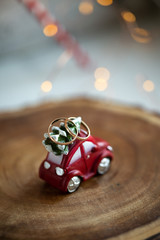 Fototapeta premium Red toy car with a christmas tree on the roof and two wedding ring, with bokeh on background. new year wedding concept