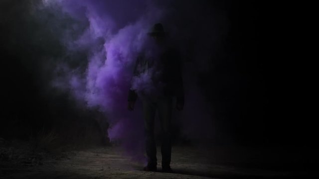 A man in a hat stands at night in the middle of purple smoke Magician