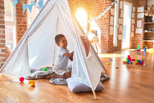 Beautiful african american toddler playing inside tipi smiling at kindergarten