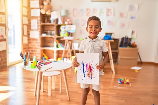 Beautiful african american toddler standing holding draw smiling at kindergarten
