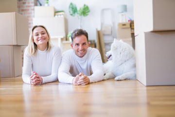 Young beautiful couple with dog lying down on the floor at new home around cardboard boxes