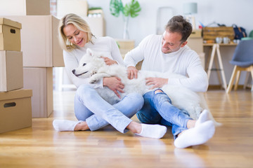 Obraz premium Young beautiful couple with dog sitting on the floor at new home around cardboard boxes