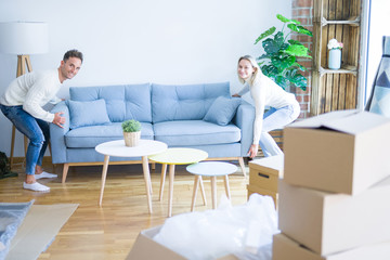 Fototapeta na wymiar Young beautiful couple moving sofa at new home around cardboard boxes