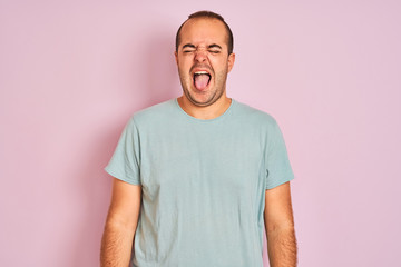 Young man wearing blue casual t-shirt standing over isolated pink background sticking tongue out happy with funny expression. Emotion concept.