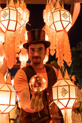 Fototapeta na wymiar Vertical photo of a tightrope walker in disguise and wearing a black hat with a crystal ball in his hand surrounded by Chinese lanterns at night.