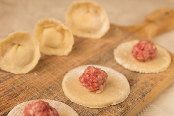 Preparation of homemade dumplings with minced meat on wooden cutting board.
