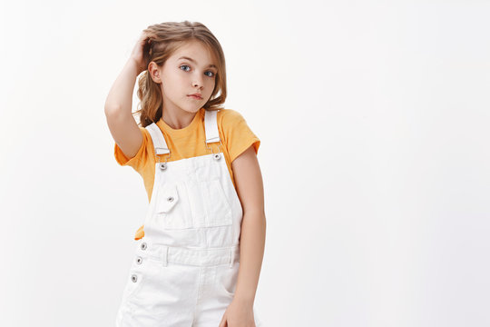 Stylish confident good-looking tender blond girl with blue eyes, tilt head posing sassy and cool, touch haircut fashionable photo, pouting silly, stand white background in yellow t-shirt, dungarees