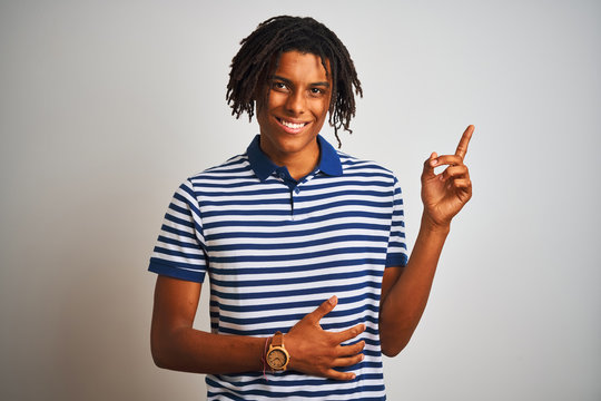 Afro man with dreadlocks wearing striped blue polo standing over isolated white background with a big smile on face, pointing with hand finger to the side looking at the camera.