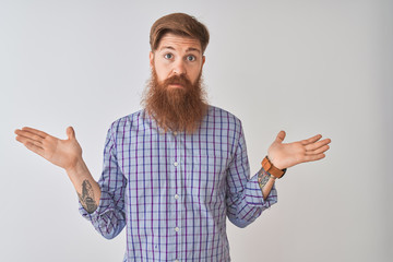 Young redhead irish man wearing casual shirt standing over isolated white background clueless and confused expression with arms and hands raised. Doubt concept.