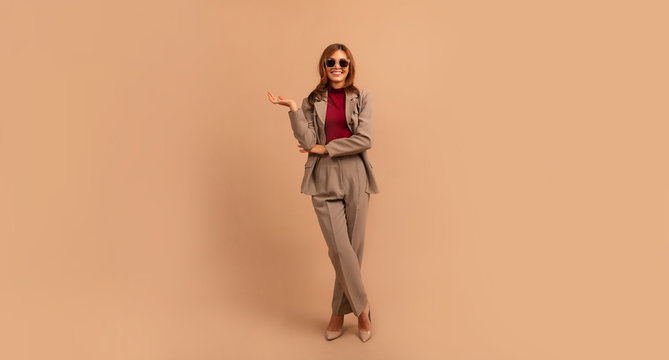Full length studio portrait of young business woman. Full length portrait of smiling attractive businesswoman in suit posing while standing with arms crossed and looking at camera isolated over beige