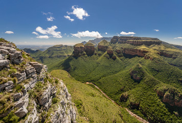 Wide angle shot of the Blyde River Canyon in South Africa as seen from a viewpoint, under a blue sky with puffy cloud