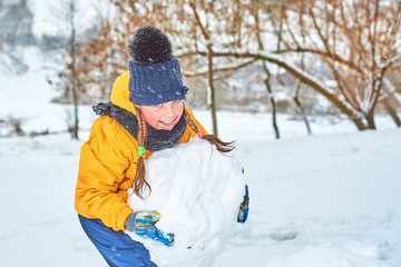 Fototapeta na wymiar little girl sculpts a snowman in winter