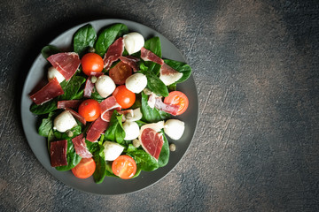 Salad with prosciutto, mozzarella, cherry tomatoes, capers and spinach on a dark plate on a dark background top view copy space.
