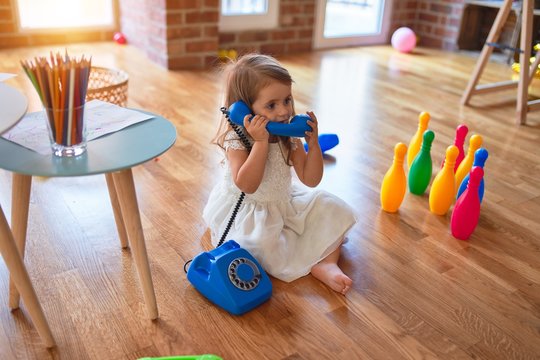 Adorable blonde toddler playing with vintage telephone. Sitting on the floor around lots of toys at kindergarten