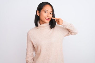 Young chinese woman wearing turtleneck sweater standing over isolated white background Pointing with hand finger to face and nose, smiling cheerful. Beauty concept