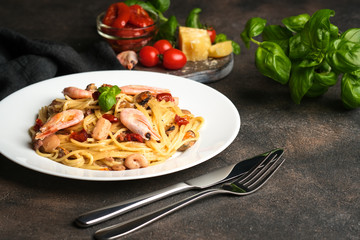 Pasta with seafood, sun-dried tomatoes, parmesan and basil on a light plate on a dark background top view copy space.