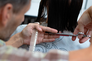 Hairdresser cutting hair and making a hairstyle to young brunette woman at the hairdresser salon. -...