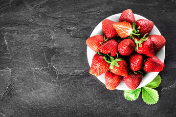 Fresh juicy strawberries on white plate on dark stone table. Red forest fruits top view on black background.