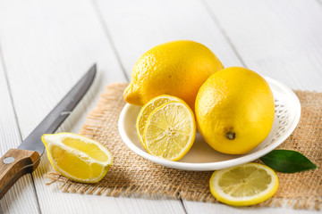 Yellow healthy fruits on wooden table. Lemons cut on jute with knife, side view.