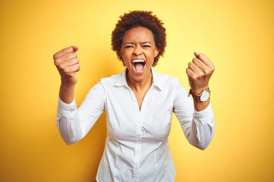 African american business woman over isolated yellow background angry and mad raising fists frustrated and furious while shouting with anger. Rage and aggressive concept.