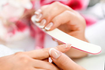 Beautician in salon applying nails art modelation. Manicure nail file in action, woman fingers on pink background.