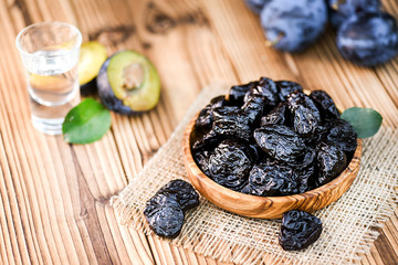 Prunes in wooden bowl on rustic table. Plum brandy or slivovitz in small glass background.