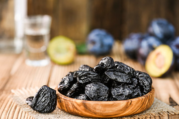 Prunes in wooden bowl on rustic table. Plum brandy or slivovitz in small glass background.