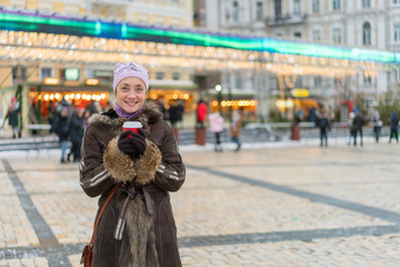 Beautiful young woman with coffee cup in the city. Beautiful woman with coffee on the street in winter clothes. Woman Having Hot Drink Outdoors On Winter Market
