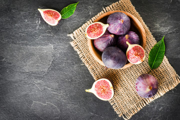 Fresh fig in rustic wood bowl top view. Cut figs fruit on dark stone table or black background with space for text.