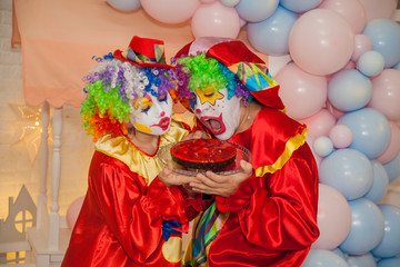 Funny clowns from the circus. Clown boy and clown girl holding a cake in their hands. The emotions of the holiday.