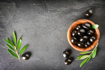 Fresh olives in wooden bowl on dark stone table. Black and green olive with pickers or sticks from...