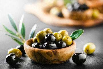 Fresh olives with core in olive bowl on dark stone table and green leaves.