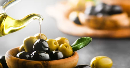 Poster Pour olive oil on ripe green and black olives in wooden bowl. Banner or panorama. © Milan
