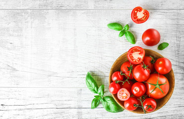 Fresh tomatoes in bowl on rustic white table top view. Tomato red background healthy food vegetables and ripe basil leaves on old board.