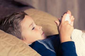 Small boy using digital tablet in bedroom.