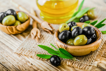 Fresh green and black olives in bowl on rustic old table. Olive oil on vintage board.