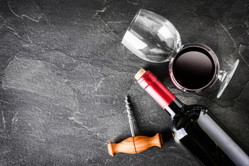 Bottle of red wine on dark stone table with copy space. Alcohol made from black grape in clear glass on black background.