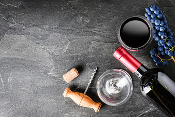 Red wine in bottle and glass on black table or dark stone board from top view. Home grape with vine...