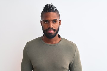 Obraz premium African american man with braids wearing green sweater over isolated white background with serious expression on face. Simple and natural looking at the camera.