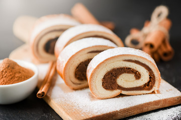Fresh baked cinnamon strudel on dark stone table sugar covered. Tasty roll cake on cut board with...