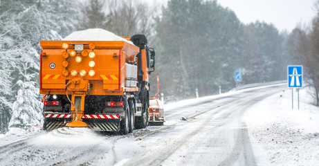 Snow plow on highway salting road. Orange truck deicing street at snowing time. Crystals dropping...